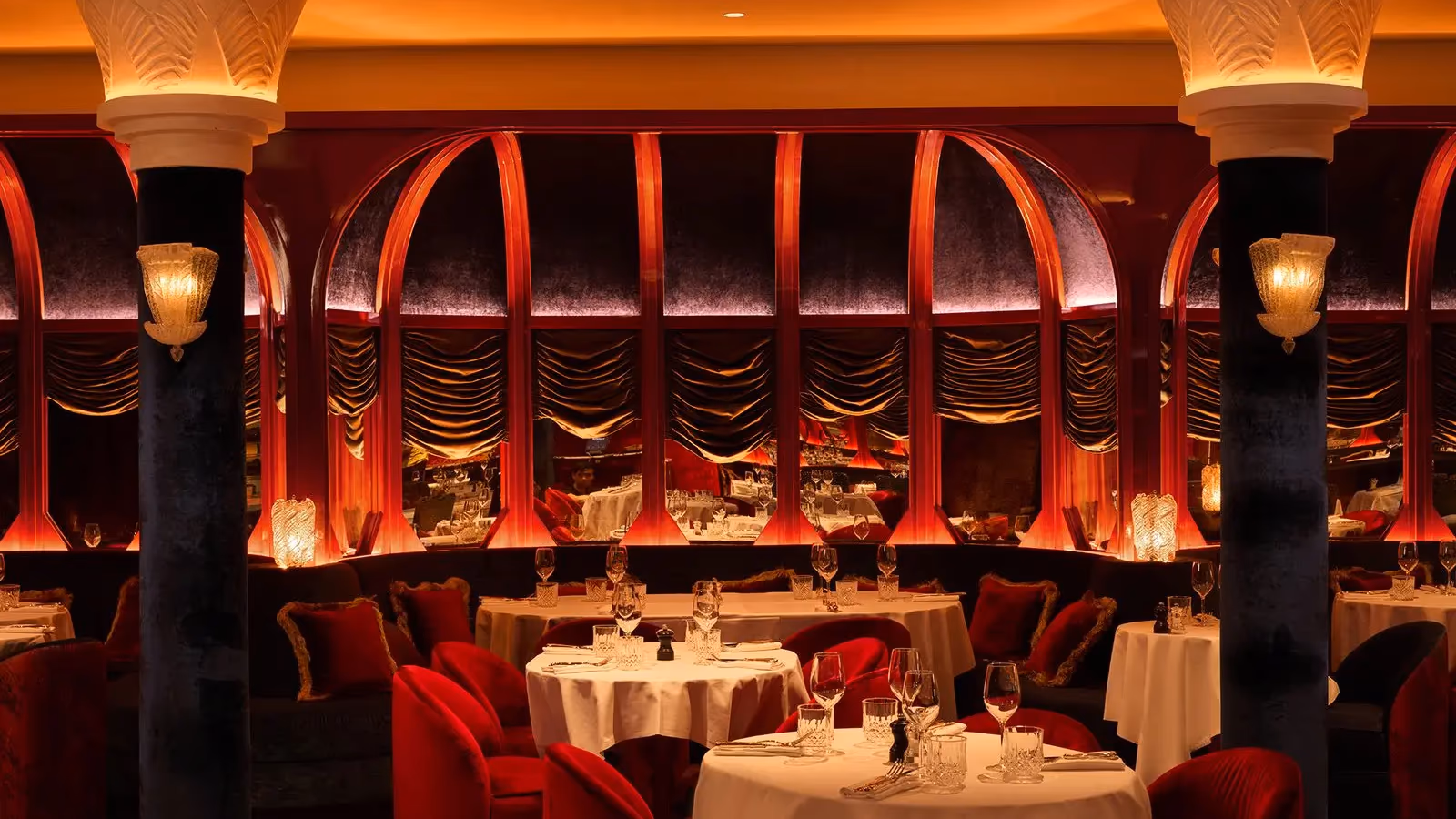 Elegant restaurant with set tables, red seats, and decorative arches lit in red and gold