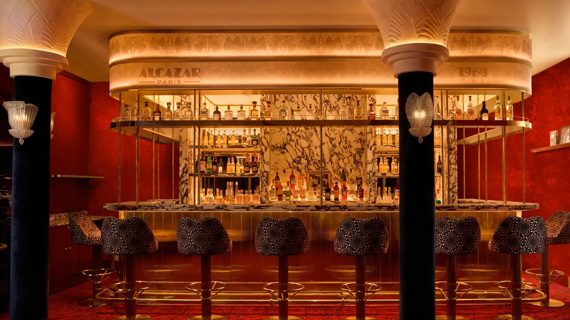 Bar avec étagères remplies de bouteilles d'alcool, tabourets à motifs et décoration murale rouge et or