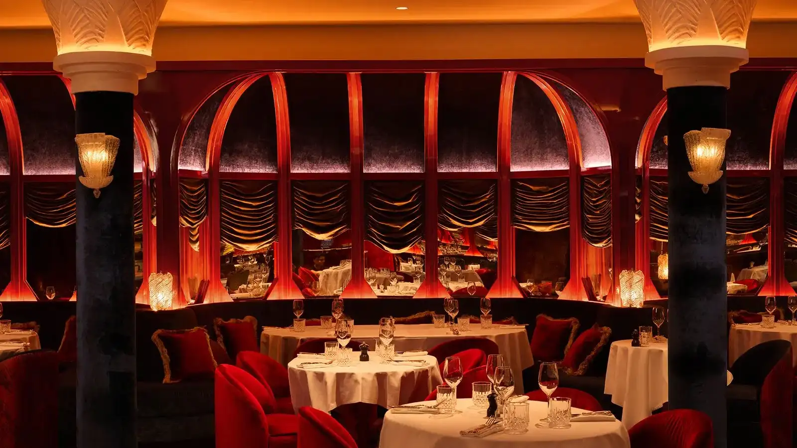 Restaurant élégant avec des tables dressées, des sièges rouges et des arches décoratives éclairées en rouge et or